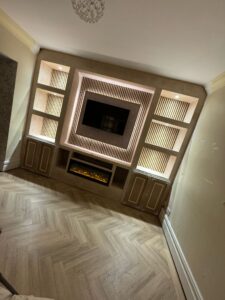 Modern living room featuring a stylish built-in entertainment unit with LED lighting, a sleek fireplace, and decorative shelving. The herringbone patterned wooden floor adds elegance to the space.