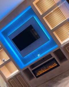 Modern living room featuring a sleek television mounted within a blue-lit wall unit, complemented by a contemporary electric fireplace below. The design emphasizes clean lines and ambient lighting, creating a stylish and inviting atmosphere.