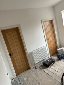 Interior view of a room featuring two wooden doors, a radiator, and construction tools on the floor, indicating ongoing renovation or home improvement.