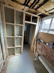 Interior view of a partially constructed room featuring wooden framing for a door and wall, with construction materials and tools visible, indicating ongoing renovation work.