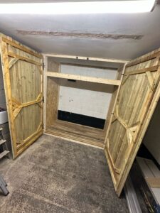 Wooden storage cabinet with open double doors, showcasing an empty interior space ready for organization or decoration. The cabinet features a rustic design, ideal for home or workshop use.