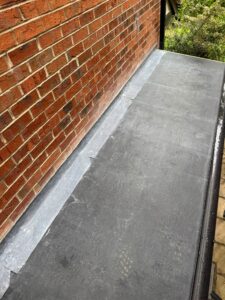 Flat roofing installation alongside a red brick wall, featuring a gray waterproof membrane and metal flashing, showcasing the transition between the roof and wall.