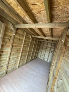 Interior view of a wooden shed showcasing unpainted wooden walls, exposed beams, and a plywood floor, ideal for storage or workshop use.